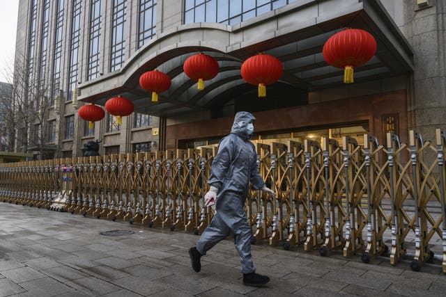 A woman wearing a protective suit and face mask walks past a closed building in Beijing