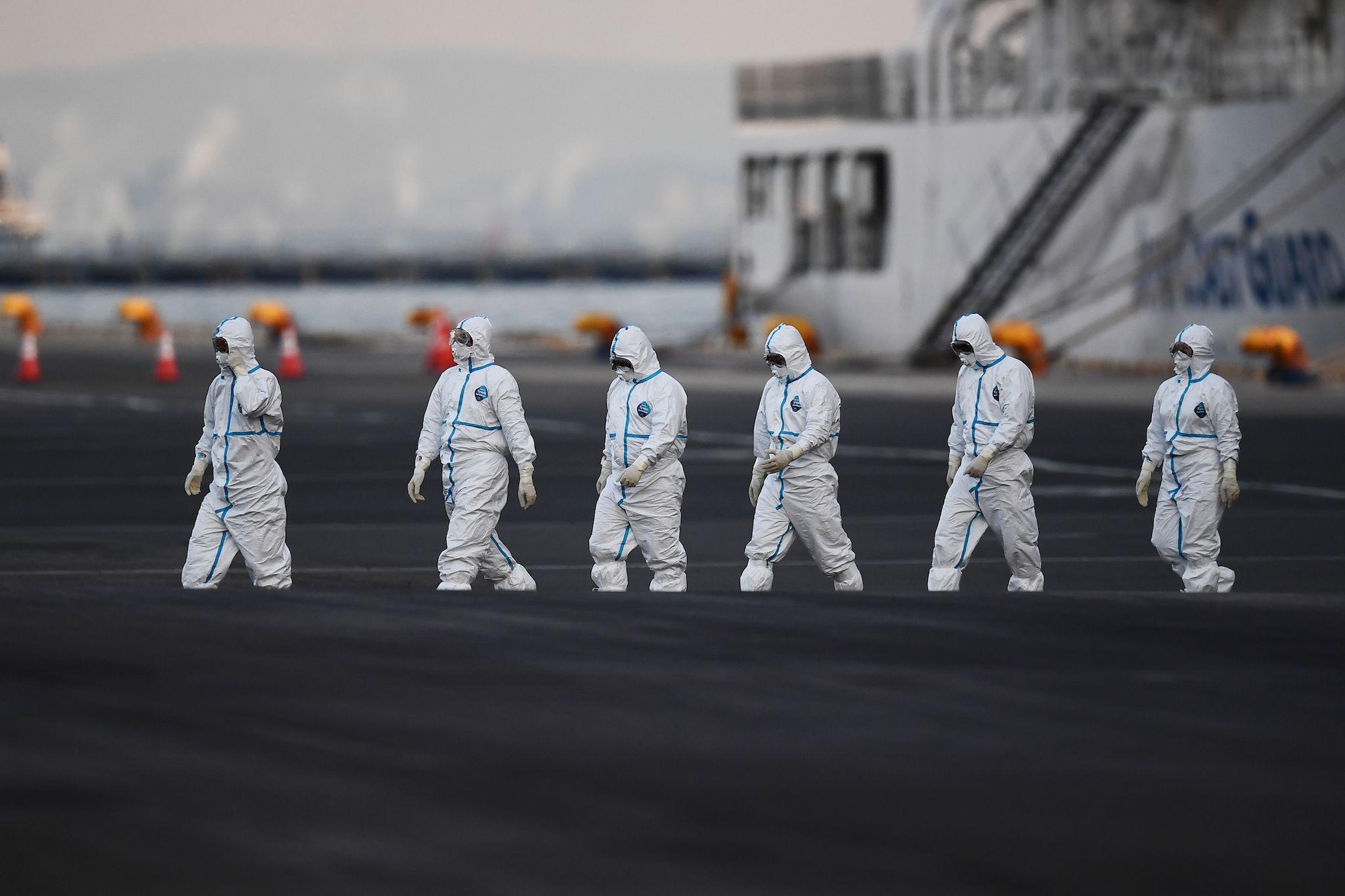 People wearing protective suits walk from the Diamond Princess cruise ship, with around 3,600 people quarantined onboard due to fears of the new coronavirus, at the Daikoku Pier Cruise Terminal in Yokohama port on February 10, 2020