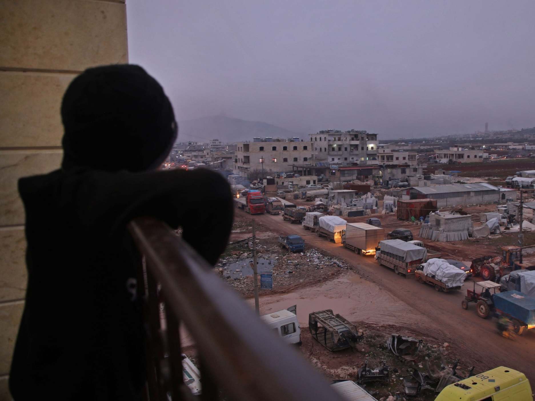 A child in the Syrian town of Dana, east of the Turkish-Syrian border in the northwestern Syrian Idlib province, watches from a balcony as a large convoy of displaced people who fled pro-regime attacks on rebel-held areas of the same province seek shelter in safer parts, on February 11, 2020.