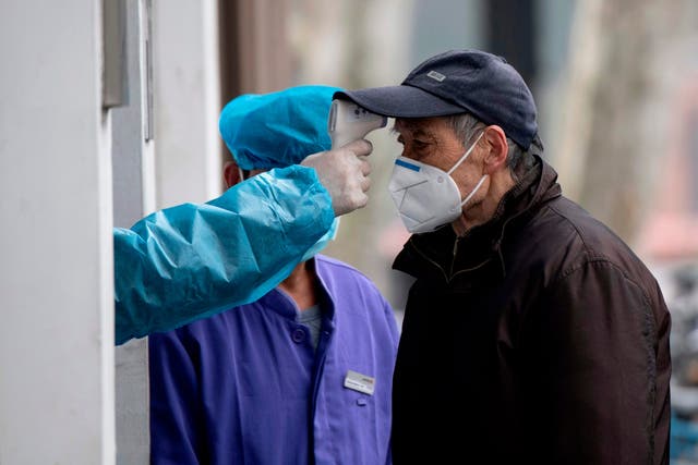 An elderly man wearing a face mask has his temperature checked before entering a community hospital in Shanghai on Thursday