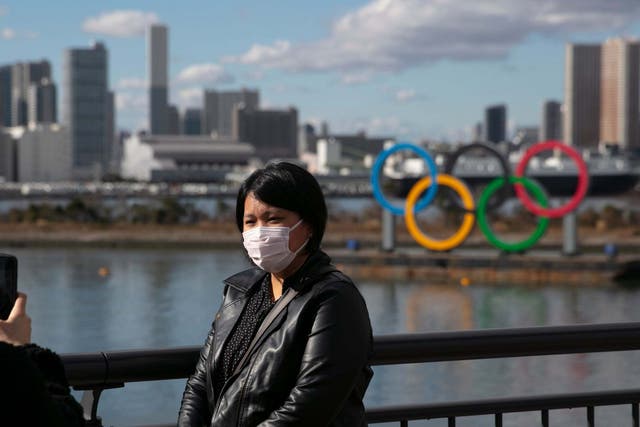 A tourist poses in front of the Olympic rings in Tokyo wearing a face mask amid the coronavirus outbreak