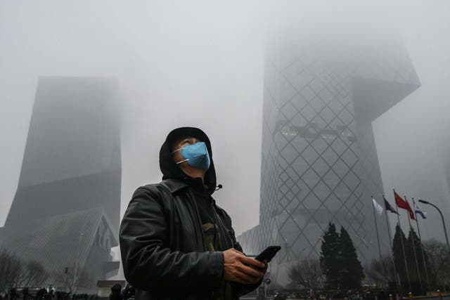 A Chinese man wears a protective mask as he stands near the CCTV building in fog and pollution during rush hour in Beijing's central business district