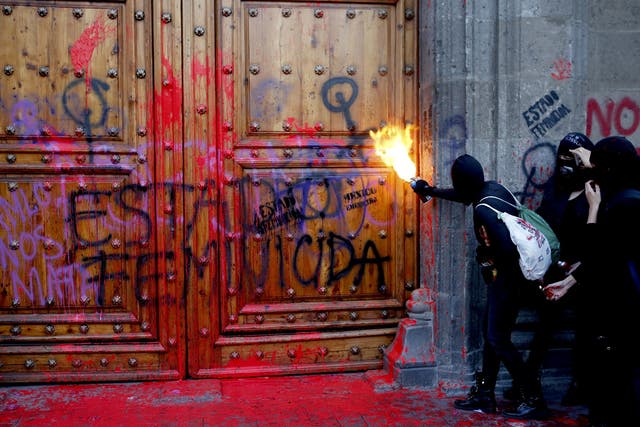 'Femicide state' is graffitied on the Mexican president's residence as a protester sprays fire at the door
