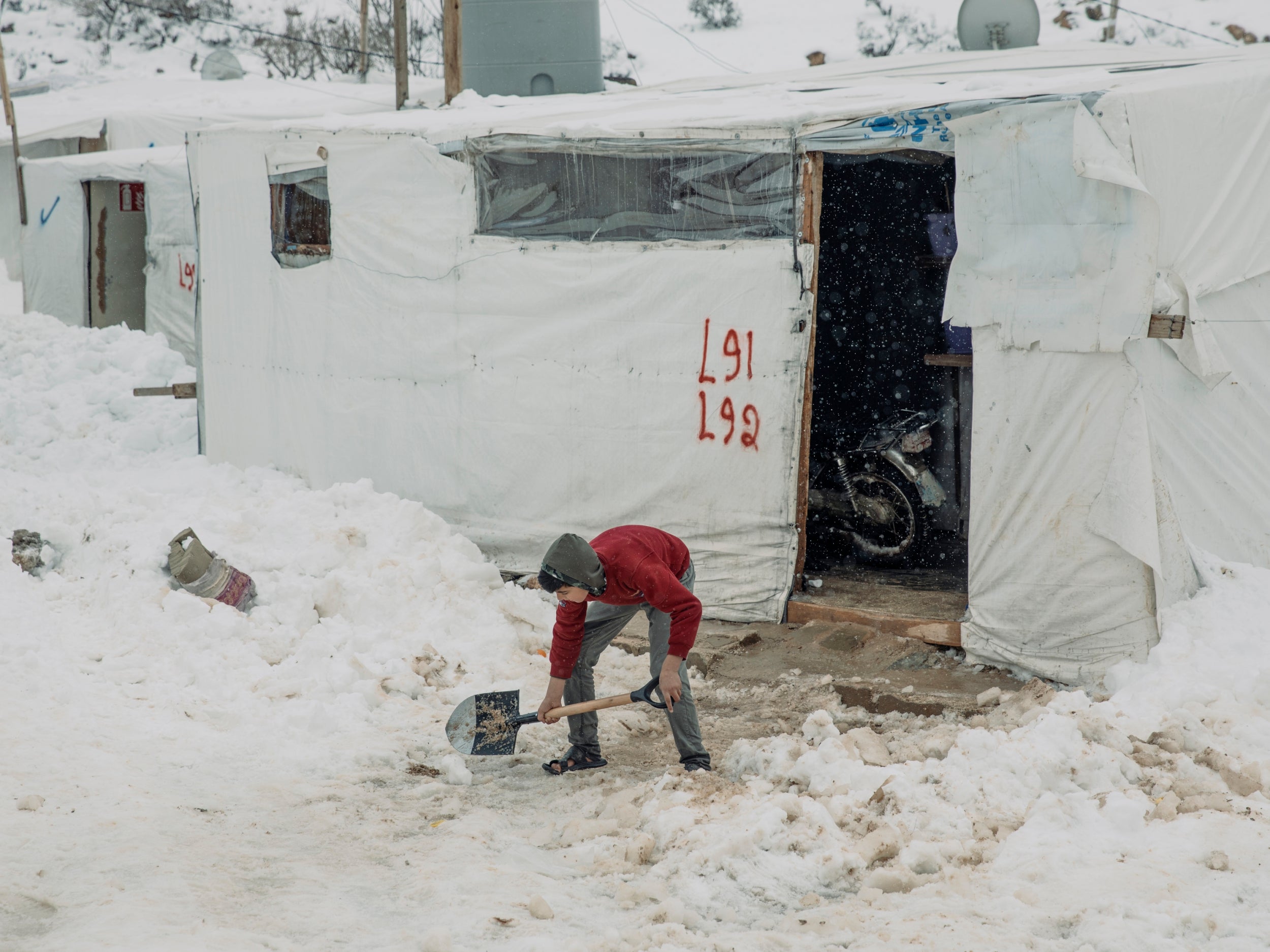 A young boy, dressed in sandals, clears the entrance to his family tent