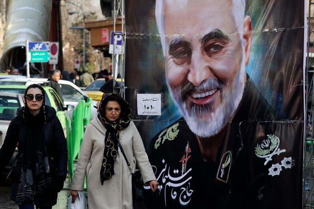 Women walk past a banner of Qassem Soleimani