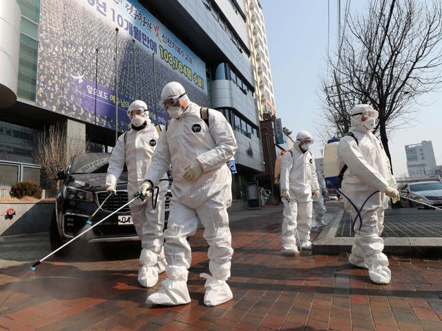 Workers wearing protective gears spray disinfectant against the new coronavirus in front of a church in Daegu