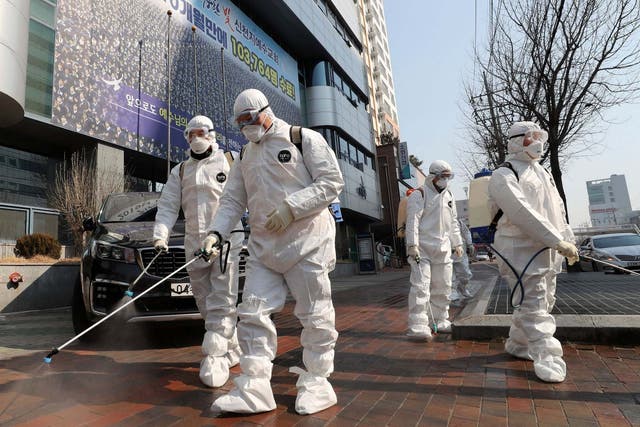 Workers wearing protective gears spray disinfectant against the new coronavirus in front of a church in Daegu