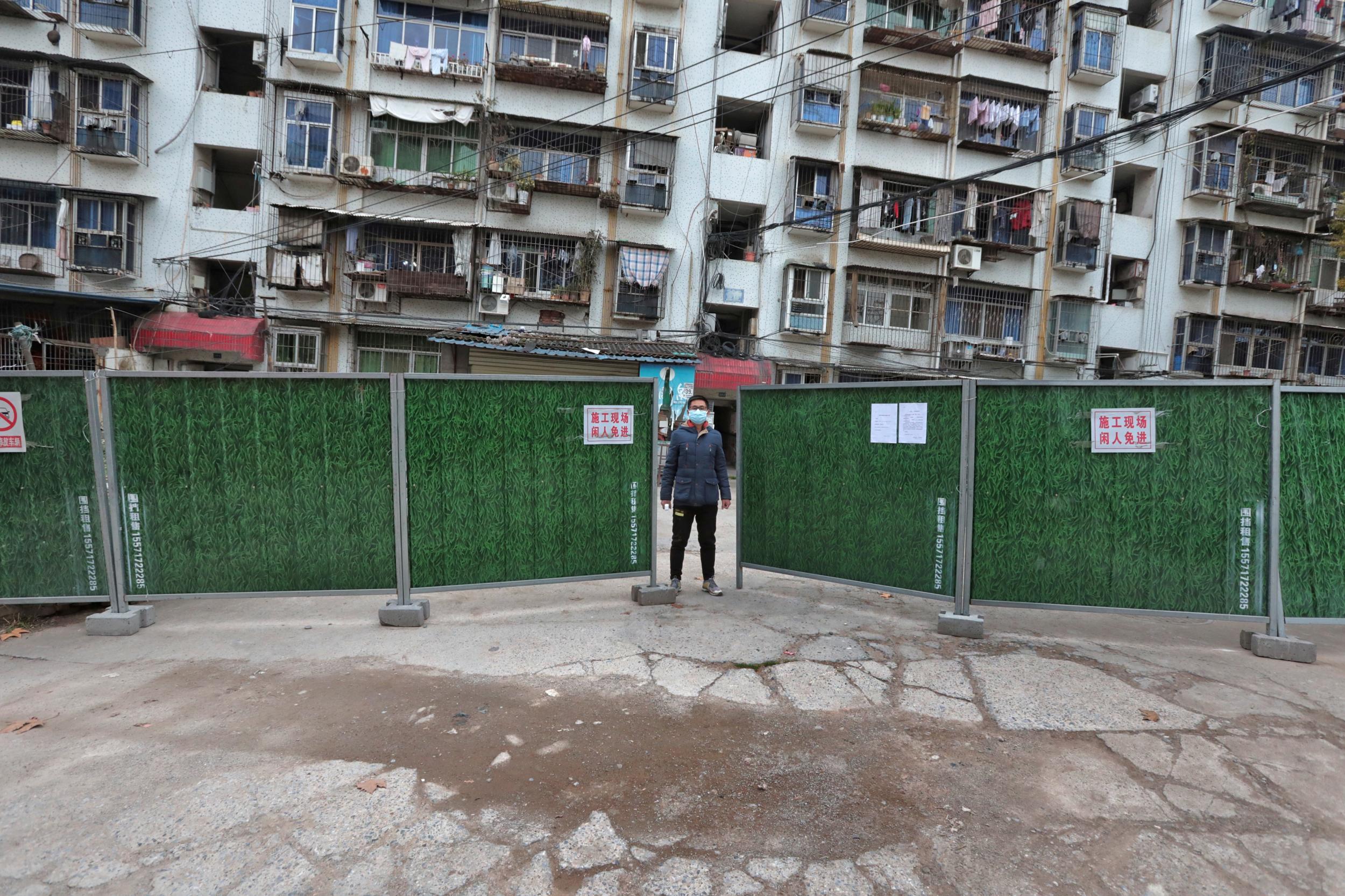 A man wearing a face mask keeps watch at an entrance to a residential community that has been fenced in with temporary barriers, in Yichang city of Hubei