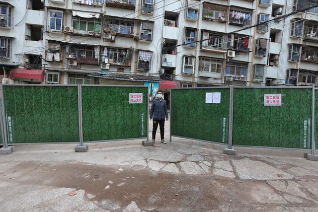 A man wearing a face mask keeps watch at an entrance to a residential community that has been fenced in with temporary barriers, in Yichang city of Hubei 10 February 2020