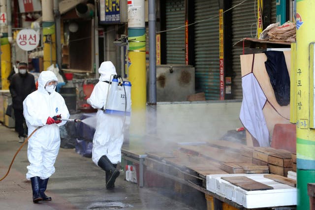 Workers wearing protective gears spray disinfectant as a precaution against the coronavirus at a local market in Busan, South Korea