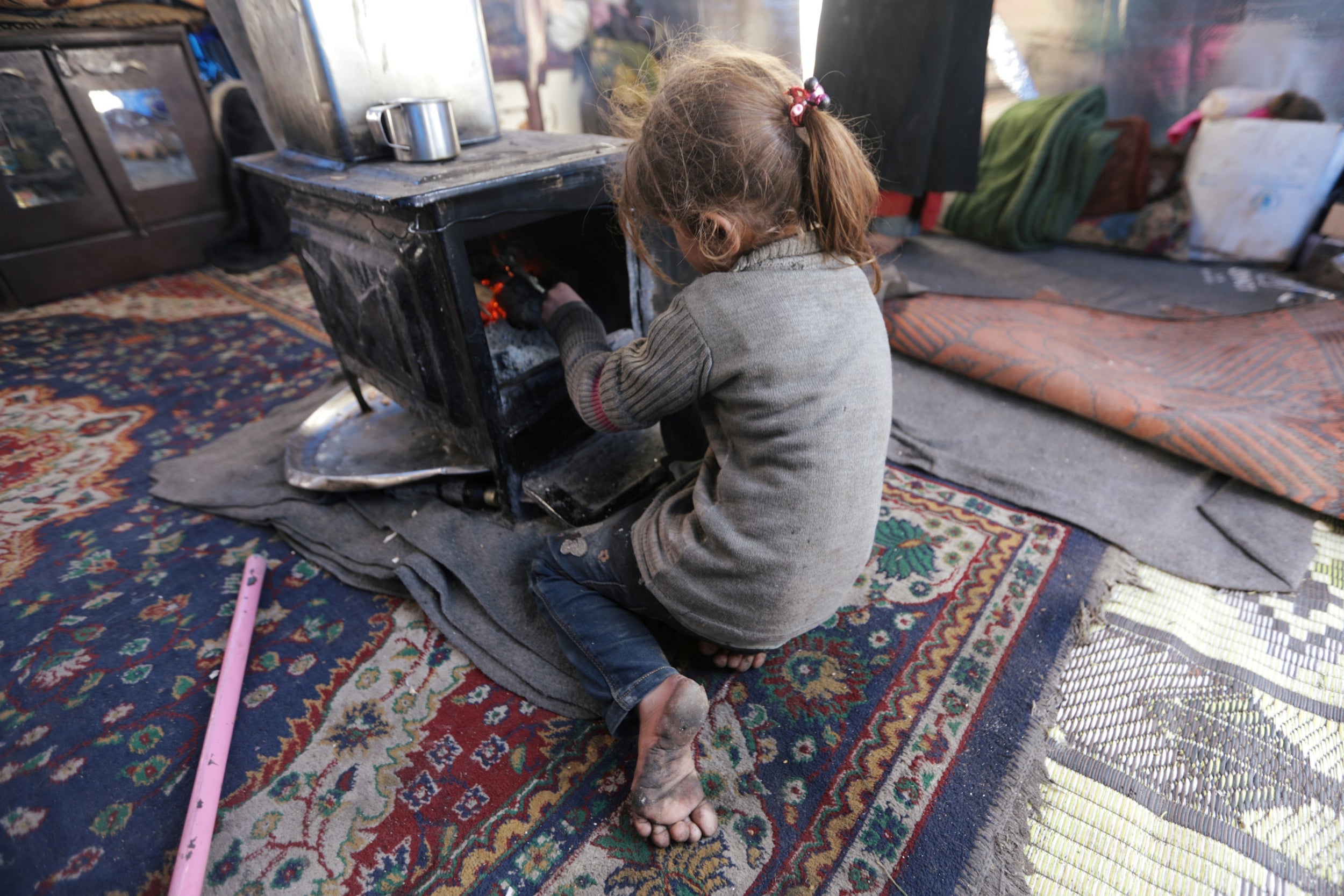 A displaced girl, who fled from western Aleppo, tries to keep warm inside her tent in Afrin