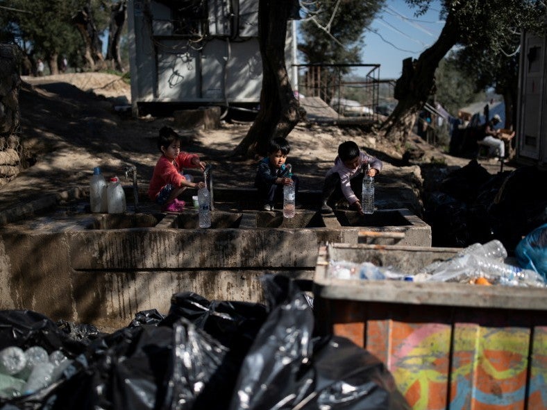 Children fill bottles with water next to piles of garbage at a makeshift camp surrounding the Moria migrant camp on the Island Lesbos Greece, 18 February 2020