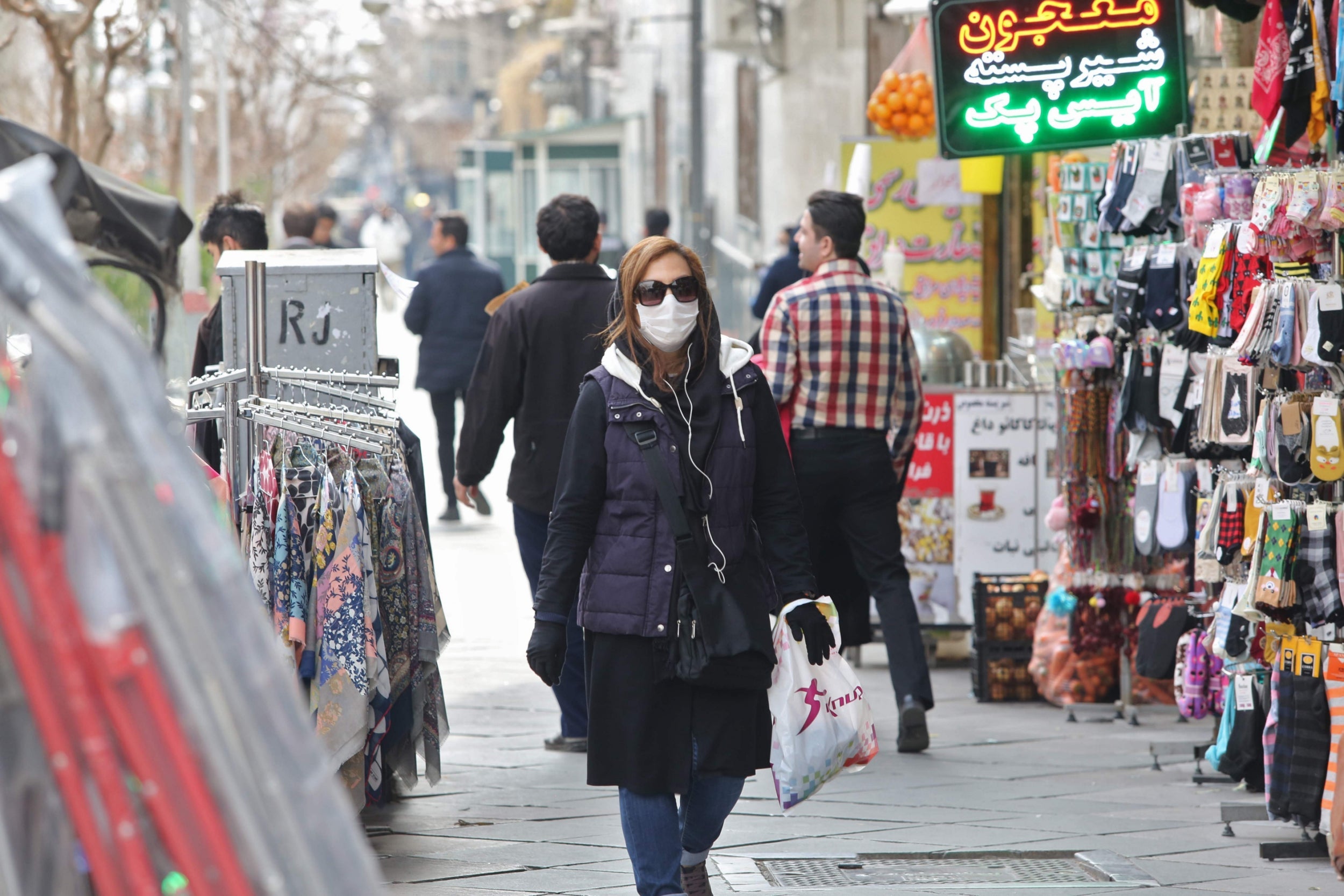 Woman wears protective mask while walking along the side of a street in the Iranian capital Tehran