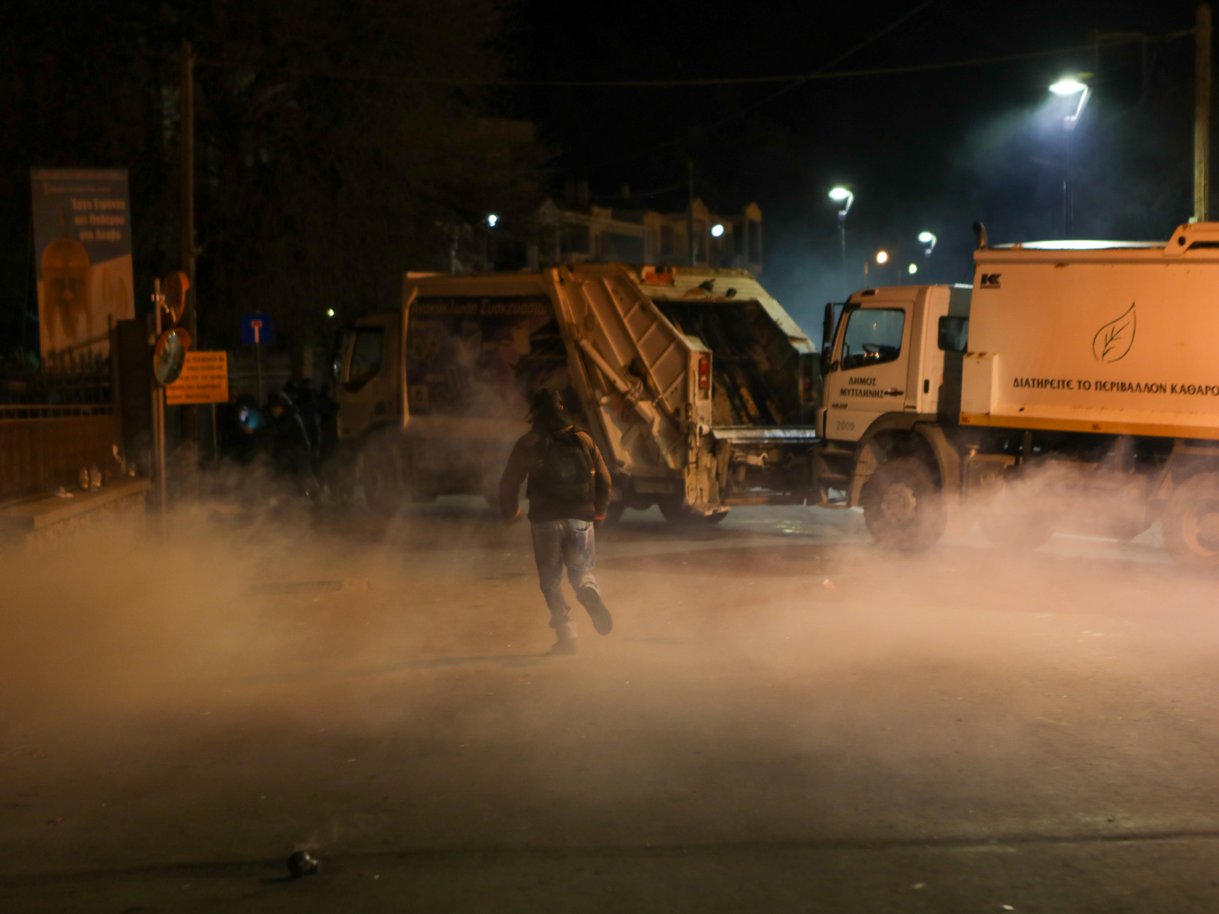 Tear gas swirls around bin lorries commandeered by protesters to block the roads