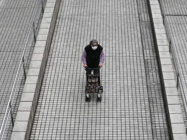 An elderly woman pushes a cart through the Tokyo Metropolitan Government building wearing a face mask