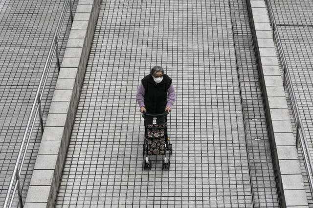 An elderly woman pushes a cart through the Tokyo Metropolitan Government building wearing a face mask