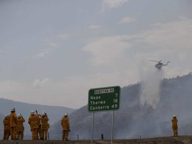 Firefighters watch as a helicopter water-bombs a fire last month