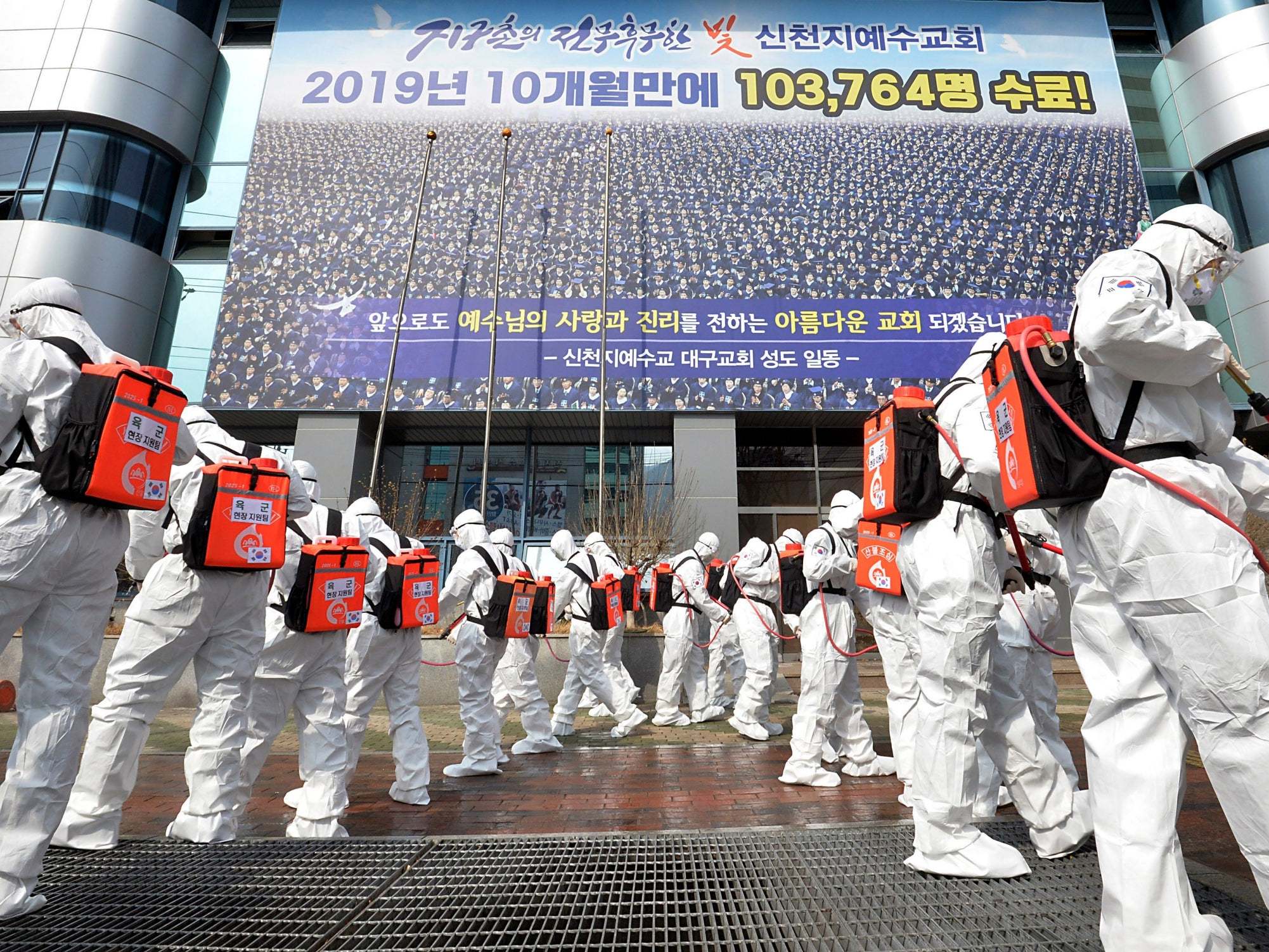 Army soldiers wearing protective suits spray disinfectant in front of a branch of the Shincheonji Church of Jesus in Daegu