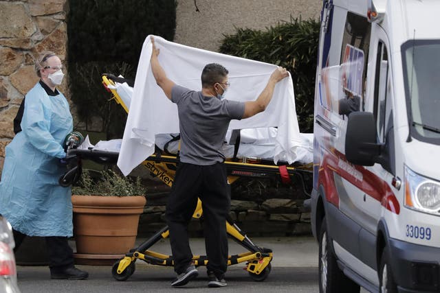A staff member blocks the view as a person is taken by a stretcher from a nursing facility near Seattle where more than 50 people are sick from the coronavirus.