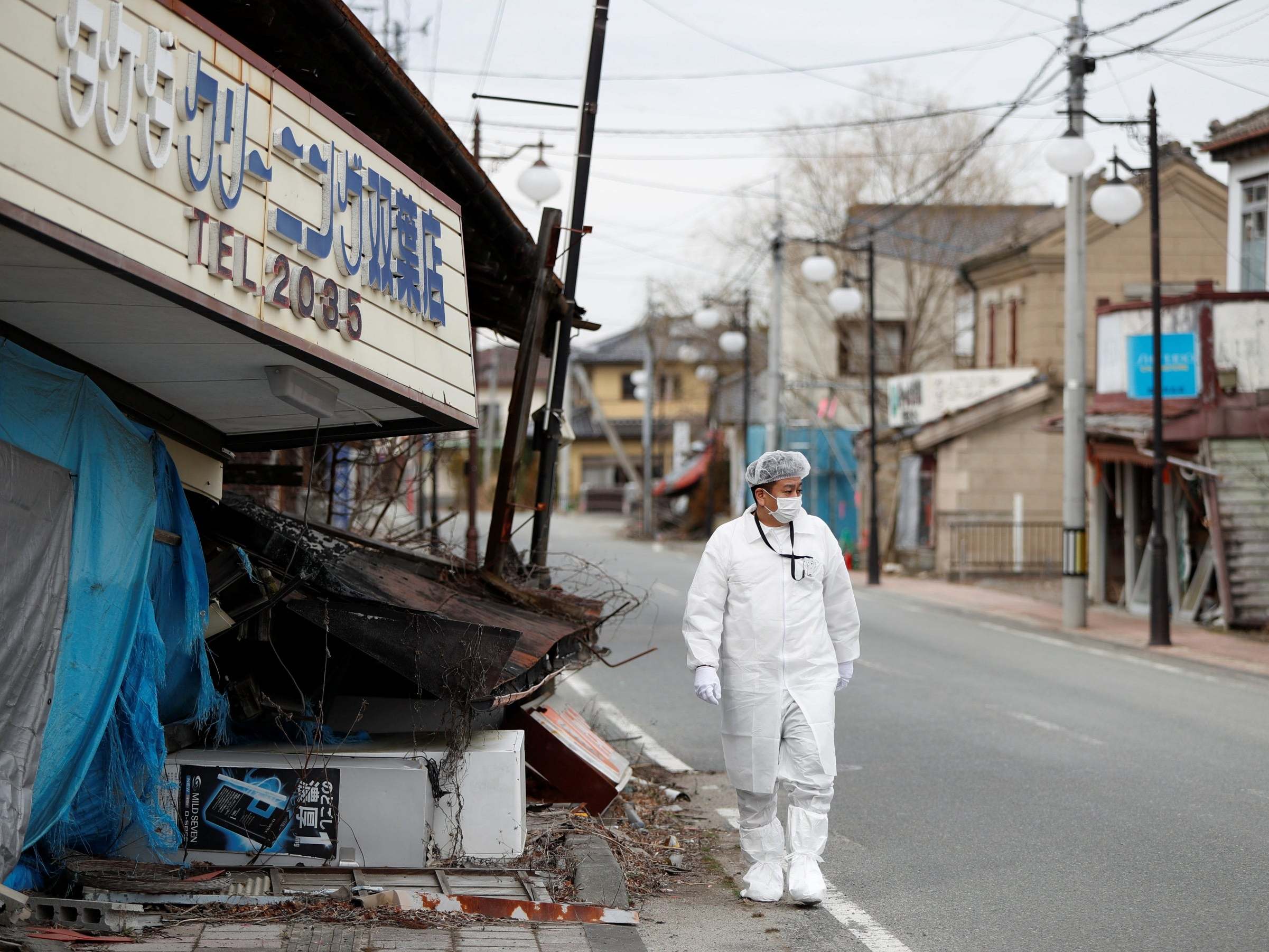 Yuji Onuma, an evacuee from Futaba Town near tsunami-crippled Fukushima Daiichi nuclear power plant, walks next to a collapsed shop on the street in Futaba Town