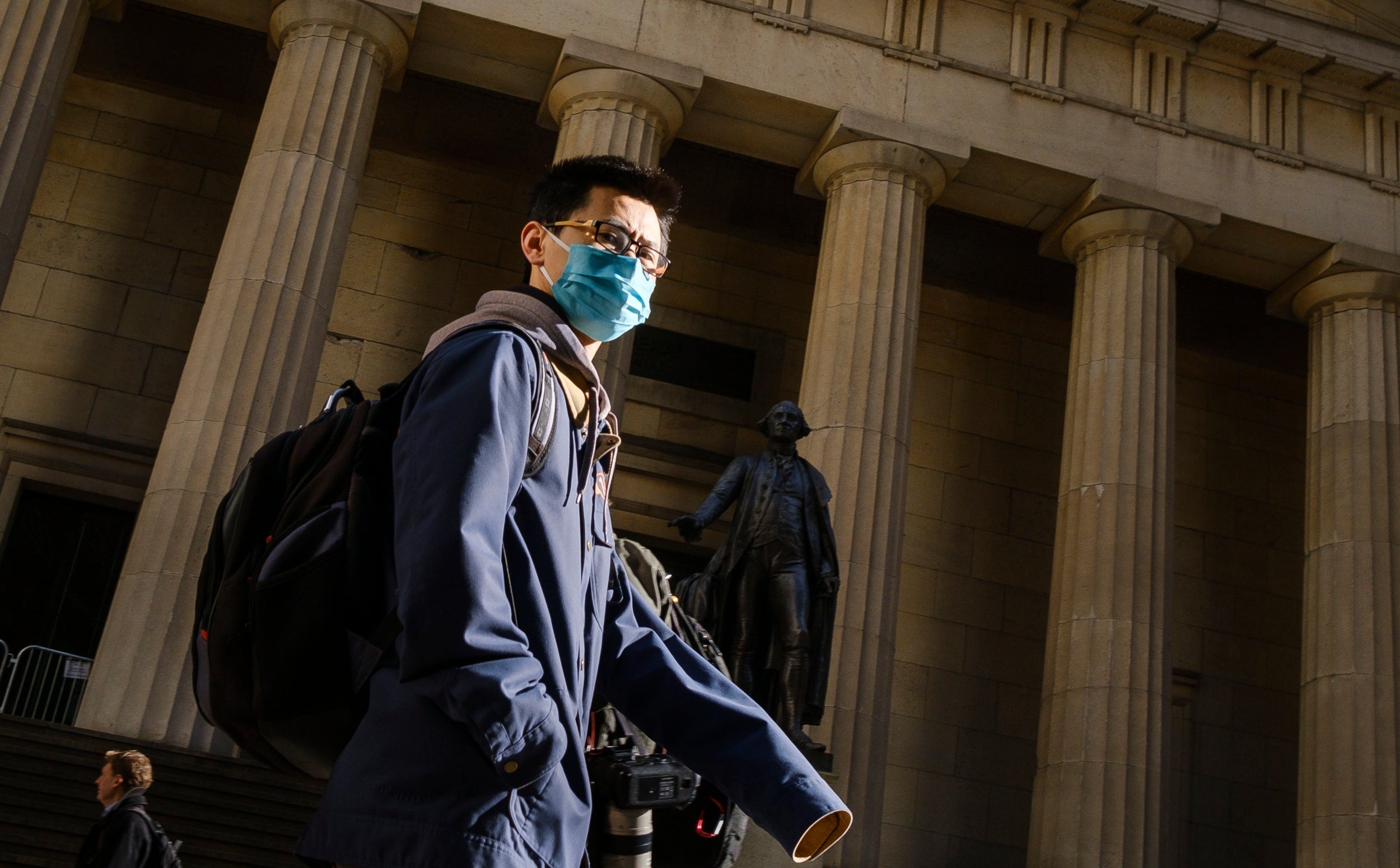 A man wearing a face mask walks down Wall Street in New York City as more cases of coronavirus emerge across the United States