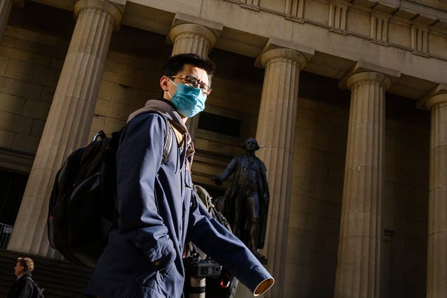 A man wearing a face mask walks down Wall Street in New York City as more cases of coronavirus emerge across the United States
