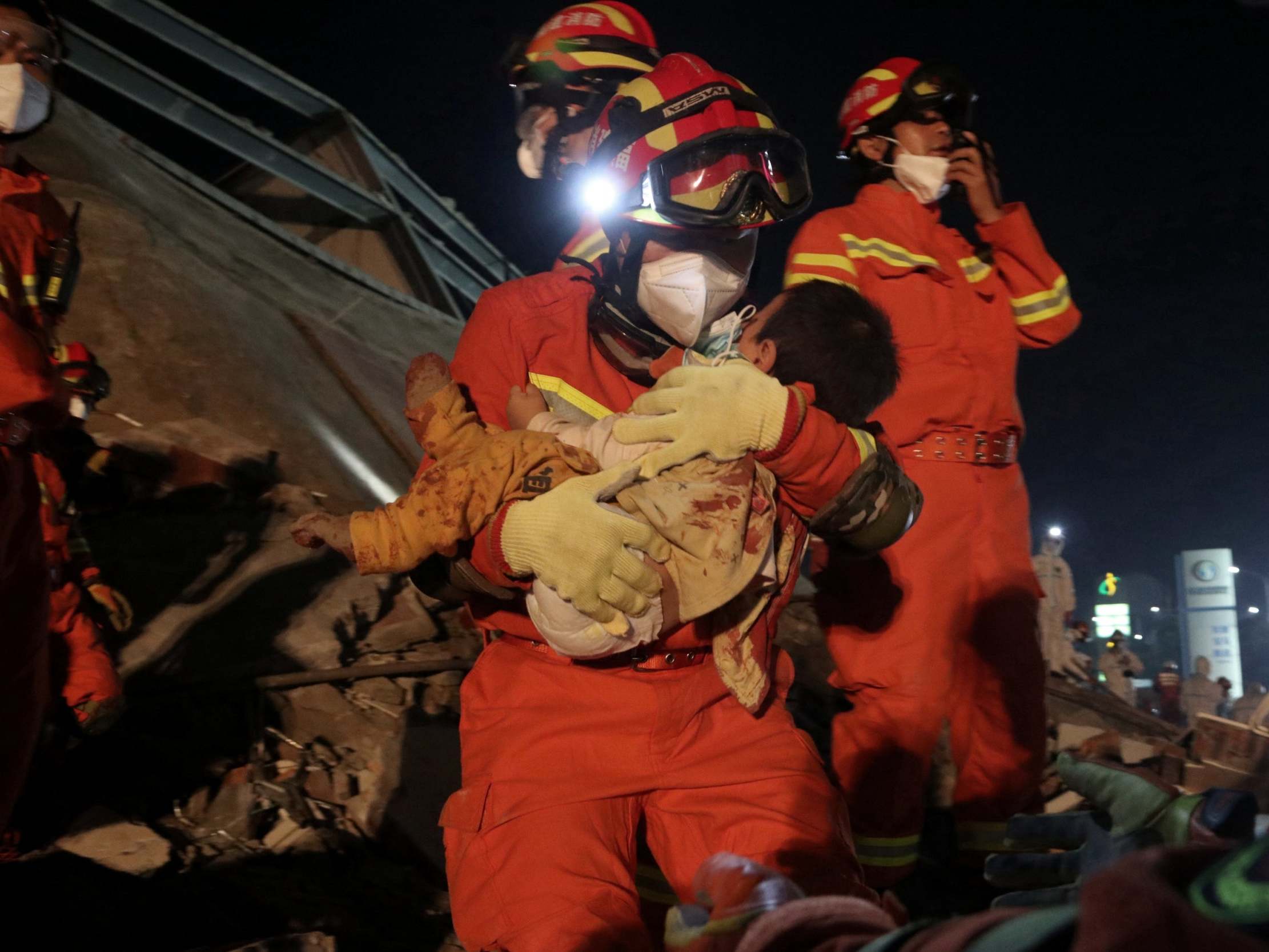 A worker wearing a face mask rescues a child from the rubble of the hotel