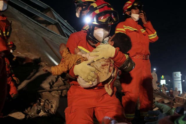 A worker wearing a face mask rescues a child from the rubble of the hotel