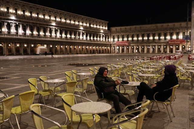 Two foreign tourists talk in a deserted San Marco Square, Venice, after Italy's prime minister announced a national emergency due to coronavirus