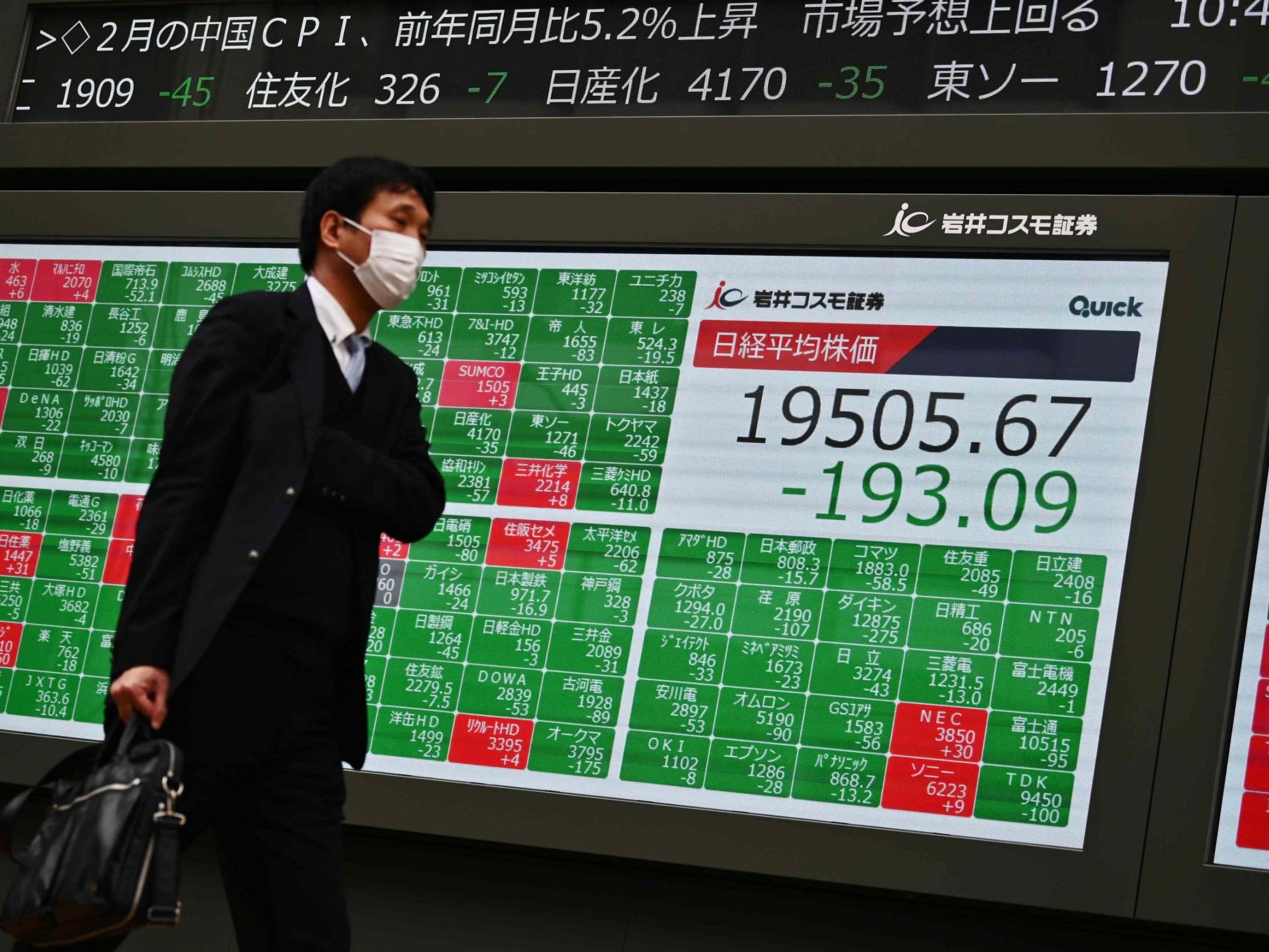 A mask-clad pedestrian passes in front of a quotation board displaying the share price numbers of the Tokyo Stock Exchange