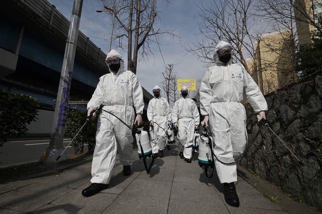 South Korean soldiers wearing protective gear spray disinfectant on the street to help prevent the spread of the Covid-19 at a residential area in Seoul on 9 March