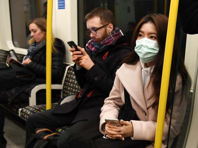 A woman wears a medical face mask while sitting on a London underground train.