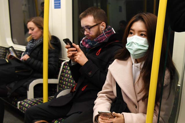 A woman wears a medical face mask while sitting on a London underground train.