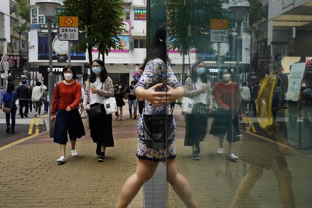People wearing face masks walk at a street in Hong Kong Friday, 13 March, 2020. For most, the coronavirus causes only mild or moderate symptoms, such as fever and cough