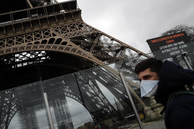 A man in a mask walks pasts the Eiffel tower, which is closed because of a ban on gatherings of more than 100 people