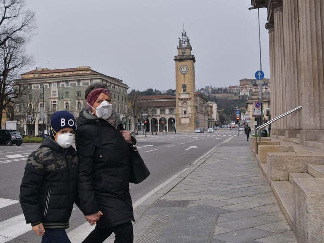 A woman and a child wearing face masks cross a road in the nearly-deserted city of Bergamo