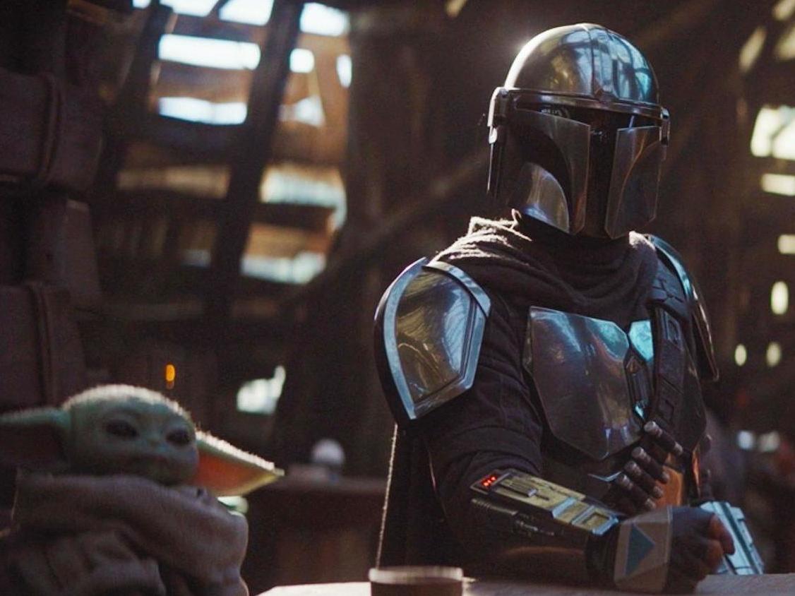 The Mandalorian (Pedro Pascal) sits with a tiny green companion in Disney's new Star Wars spin-off