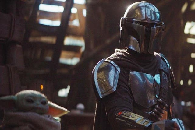 The Mandalorian (Pedro Pascal) sits with a tiny green companion in Disney's new Star Wars spin-off
