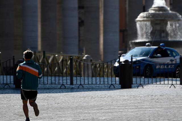 A man jogs on the Italian side as as a car of the Italian National police patrols St. Peter's Square in the Vatican as seen from Rome during the lockdown within the new coronavirus pandemic