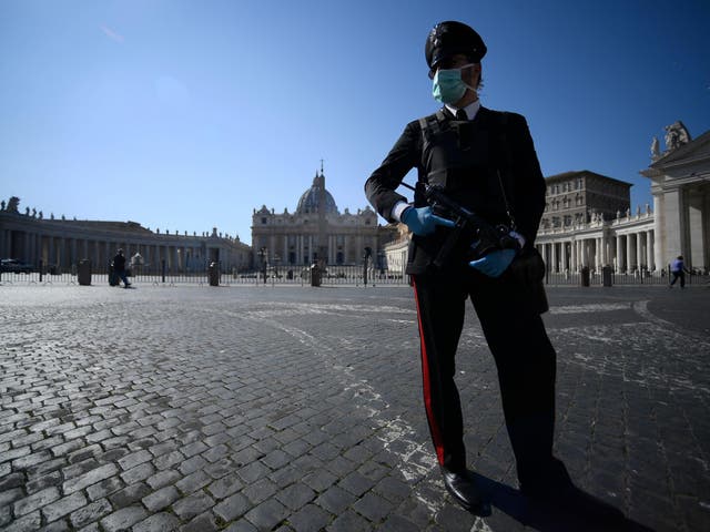 An armed Carabinieri police officer, wearing a face mask, patrols a closed and deserted St. Peter's Square in the Vatican during the lockdown within the new coronavirus pandemic