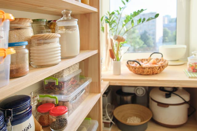 Wooden shelves with food and utensils, kitchen appliances in the pantry.