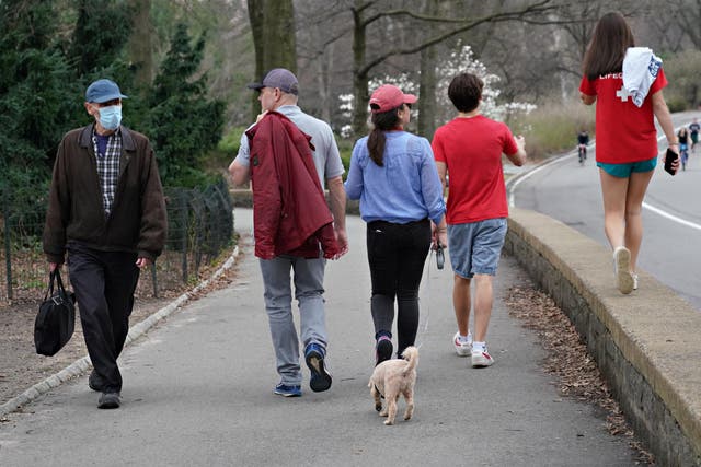 A man in a protective mask walks by a family in Central Park as the coronavirus continues to spread across the United States