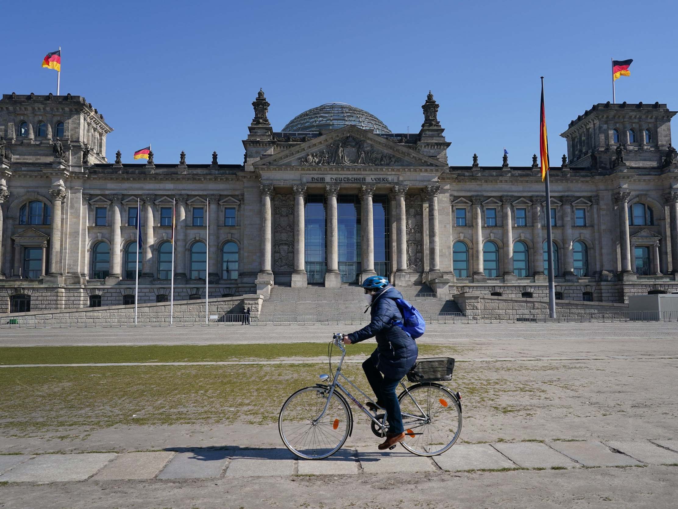 A woman wearing a protective mask rides a bicycle past the Reichstag