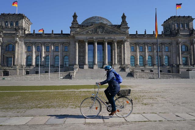 A woman wearing a protective mask rides a bicycle past the Reichstag