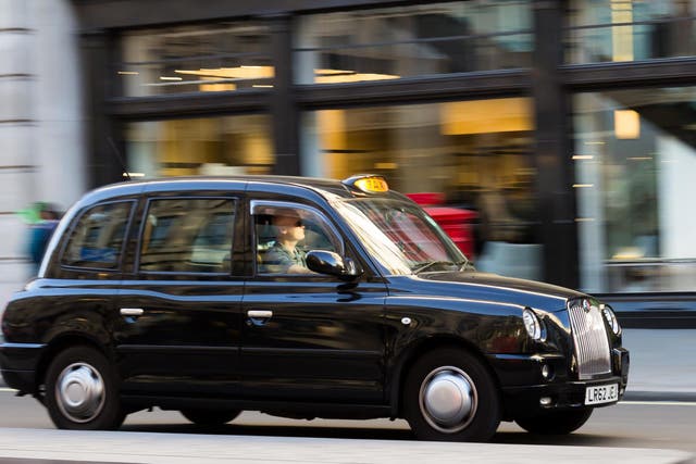 A Taxi moving down a street in London with shop windows in the background