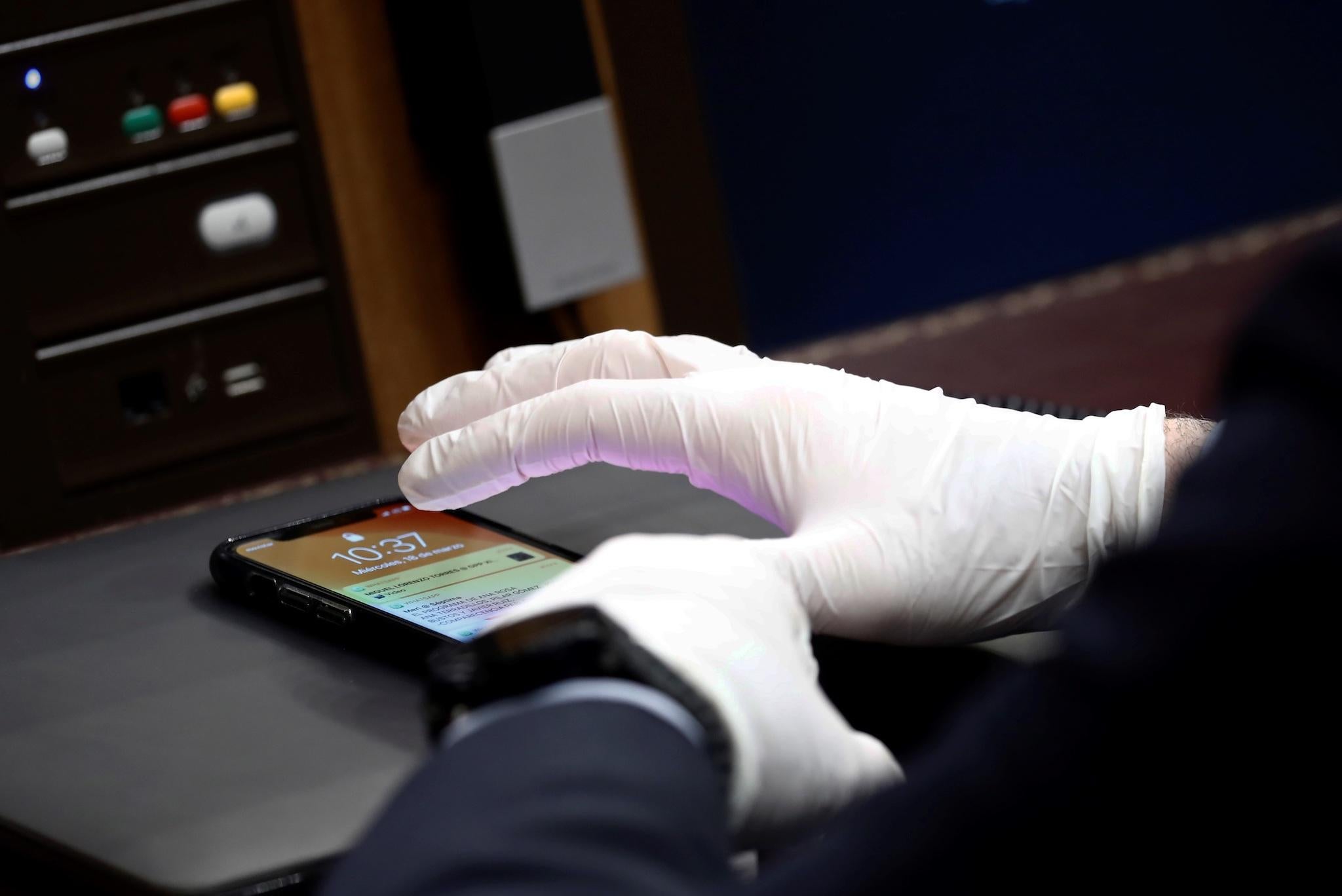 A Member of Parliament using protective gloves uses a smartphone during a session at the Spanish Parliament in Madrid to explain the Government's declaration of a State of Alert and the measures taken to mitigate the coronavirus COVID-19 consequences on March 18, 2020