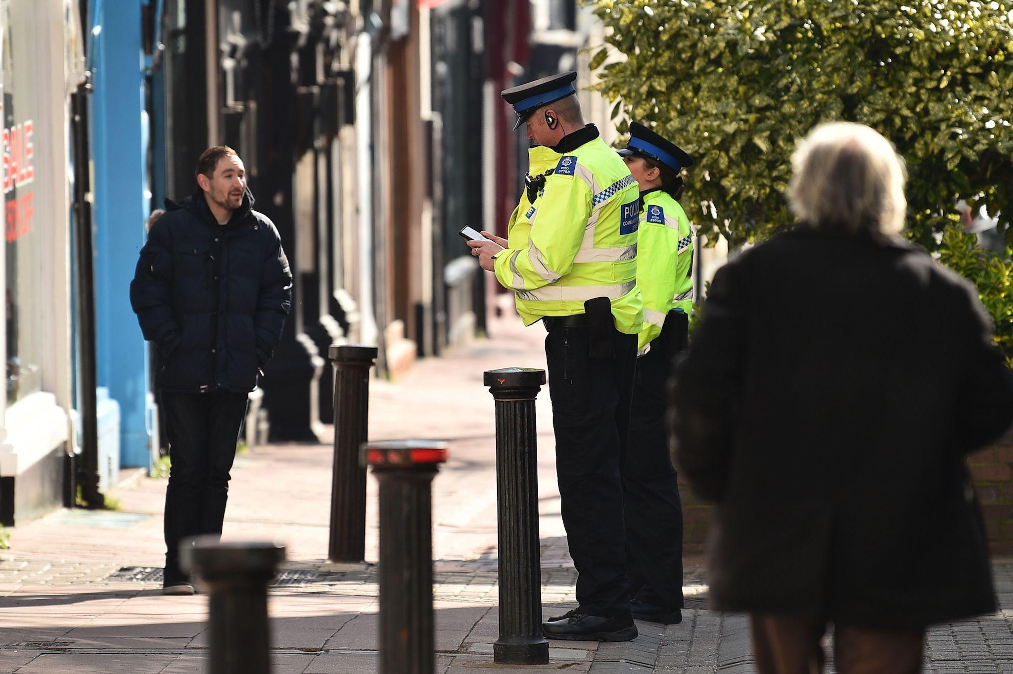 Police community support officers talk to a man on a street in Brighton shortly after the lockdown