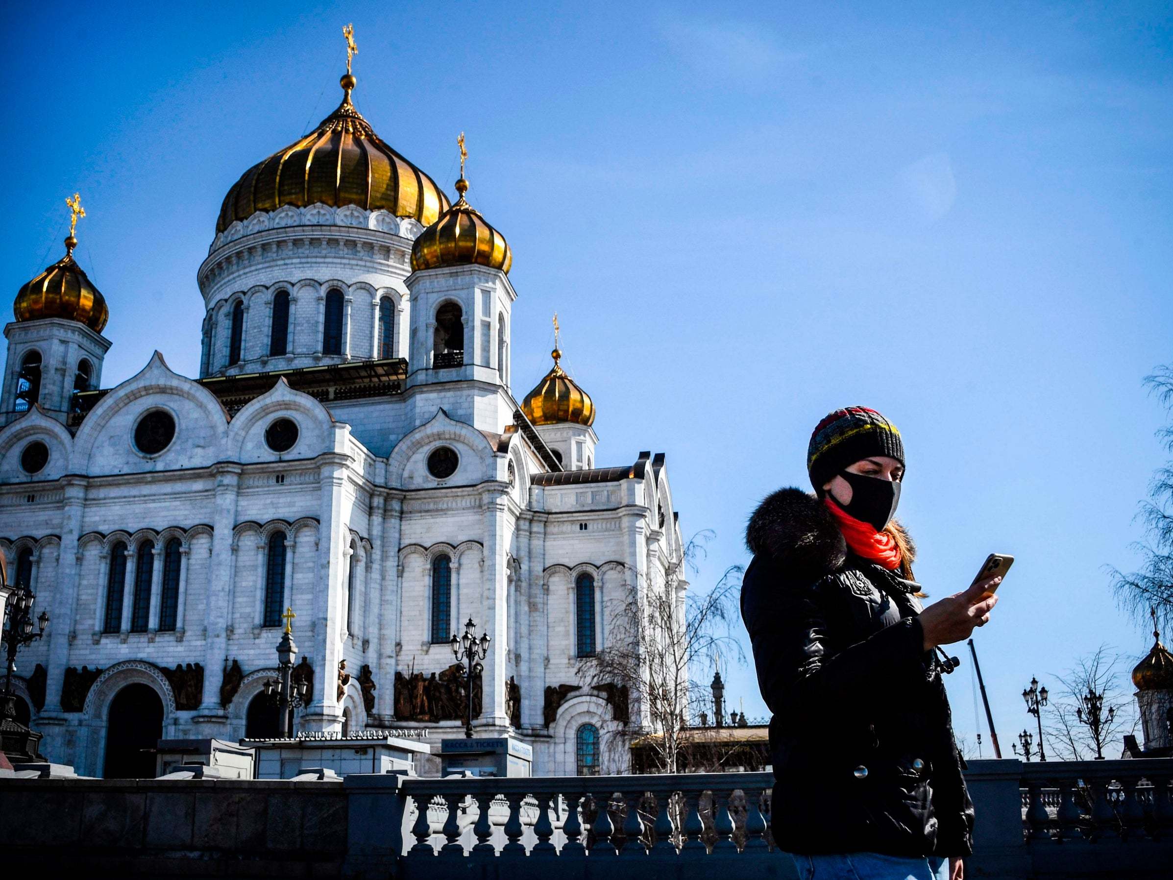 A woman wearing a mask walks past the Cathedral of Christ the Saviour in central Moscow