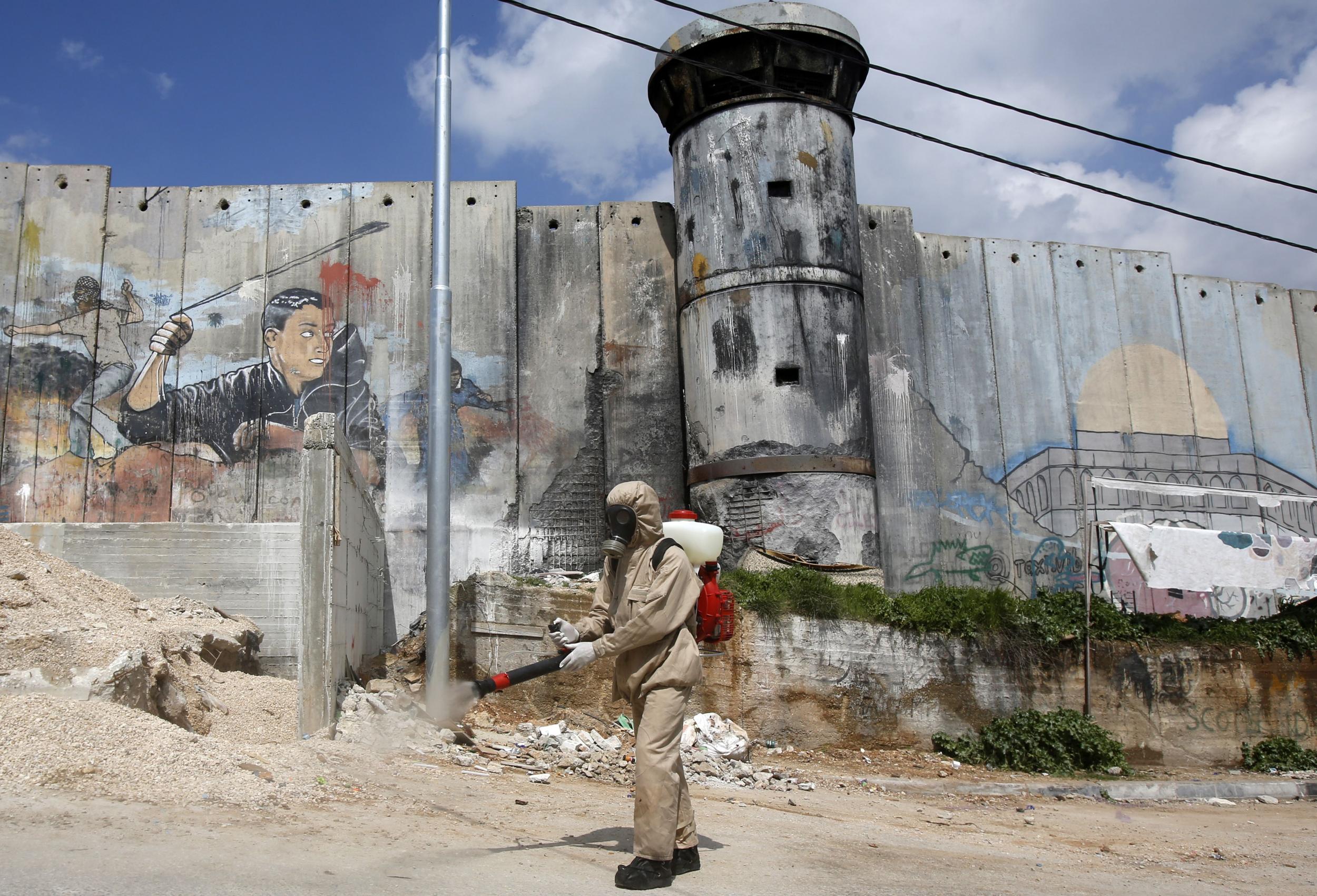 A Palestinian sanitary department worker disinfects the refugee camp of Aida, with Israel’s controversial separation barrier in the background (AFP)