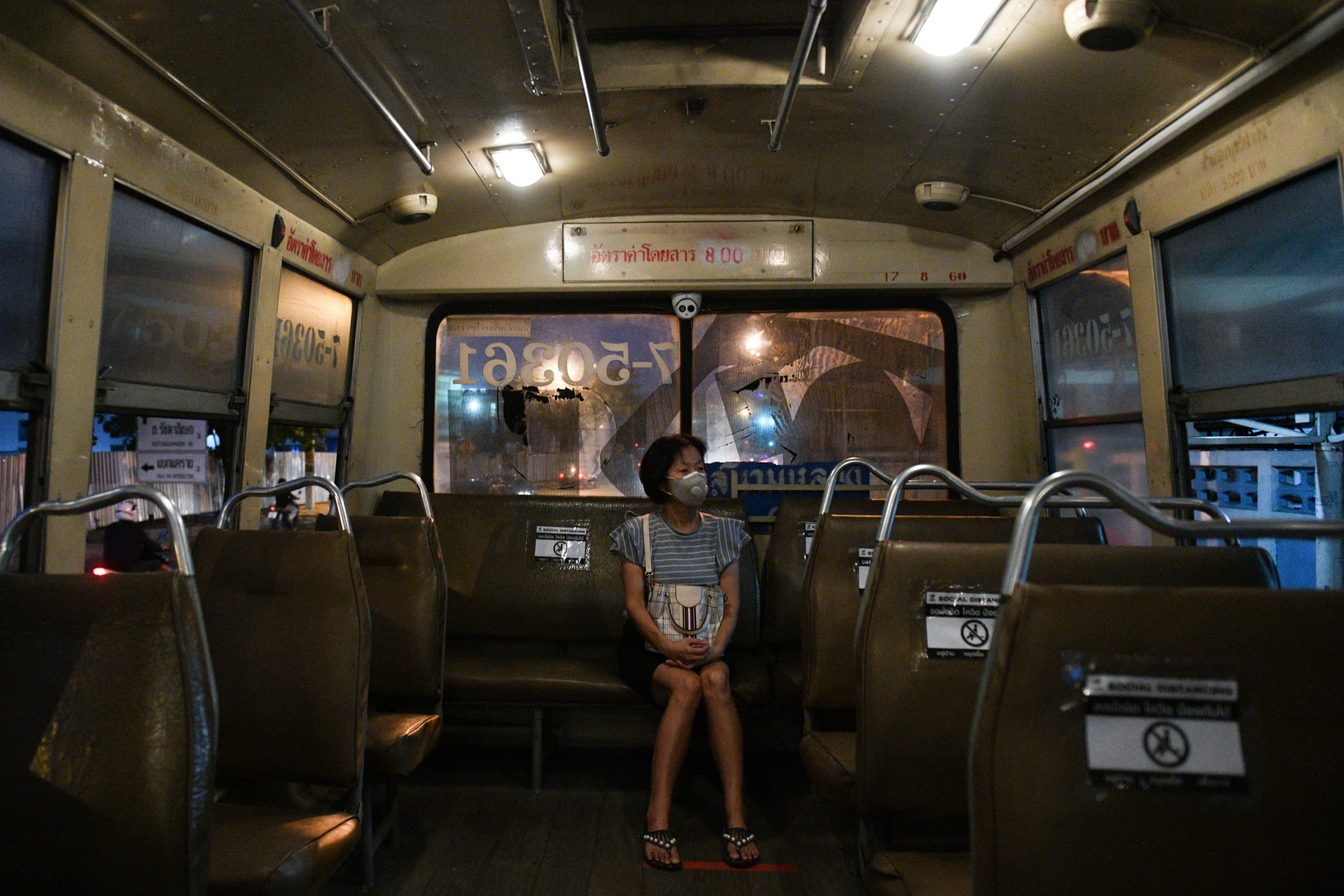 A masked woman sits alone on the back of a bus in Bangkok